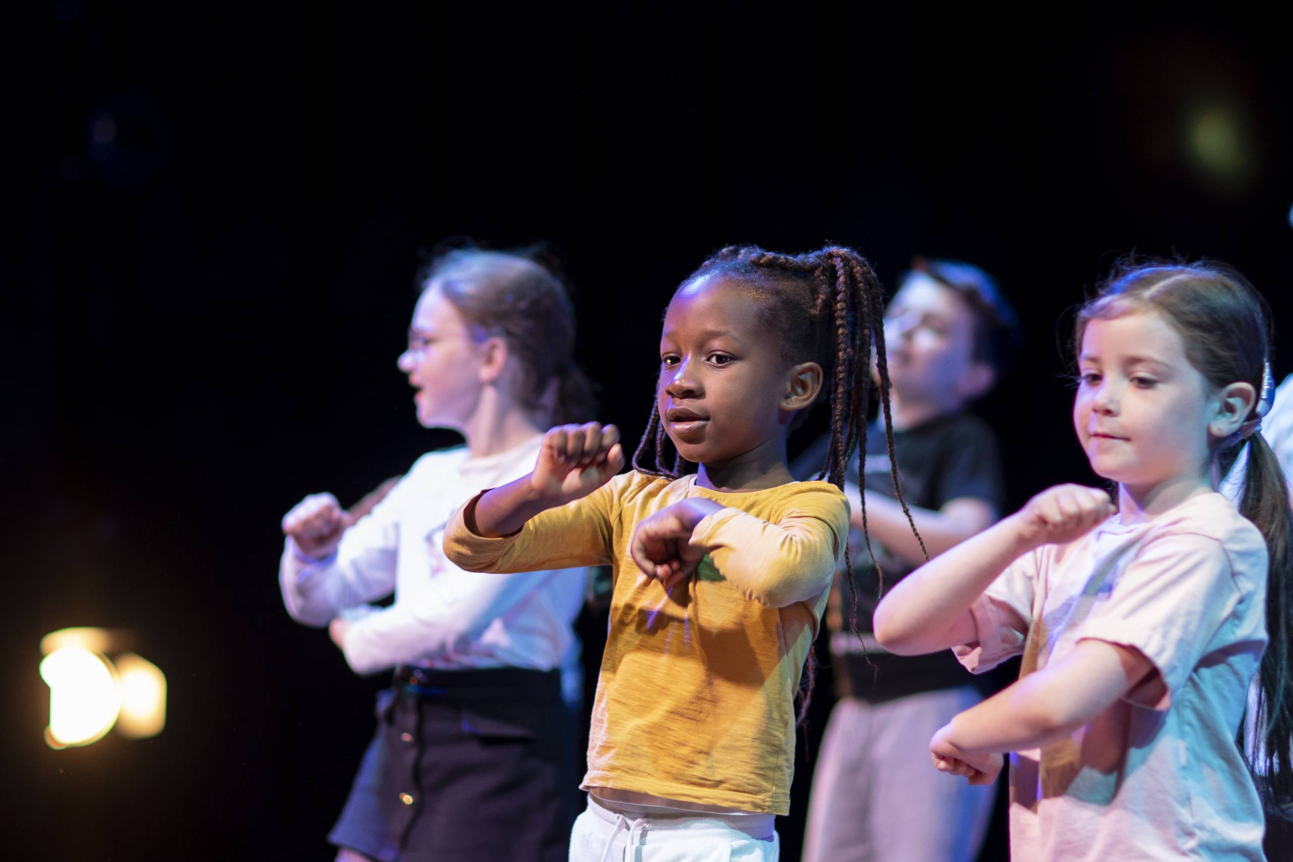 A group of four children dance to music at a workshop held in a theatre studio space