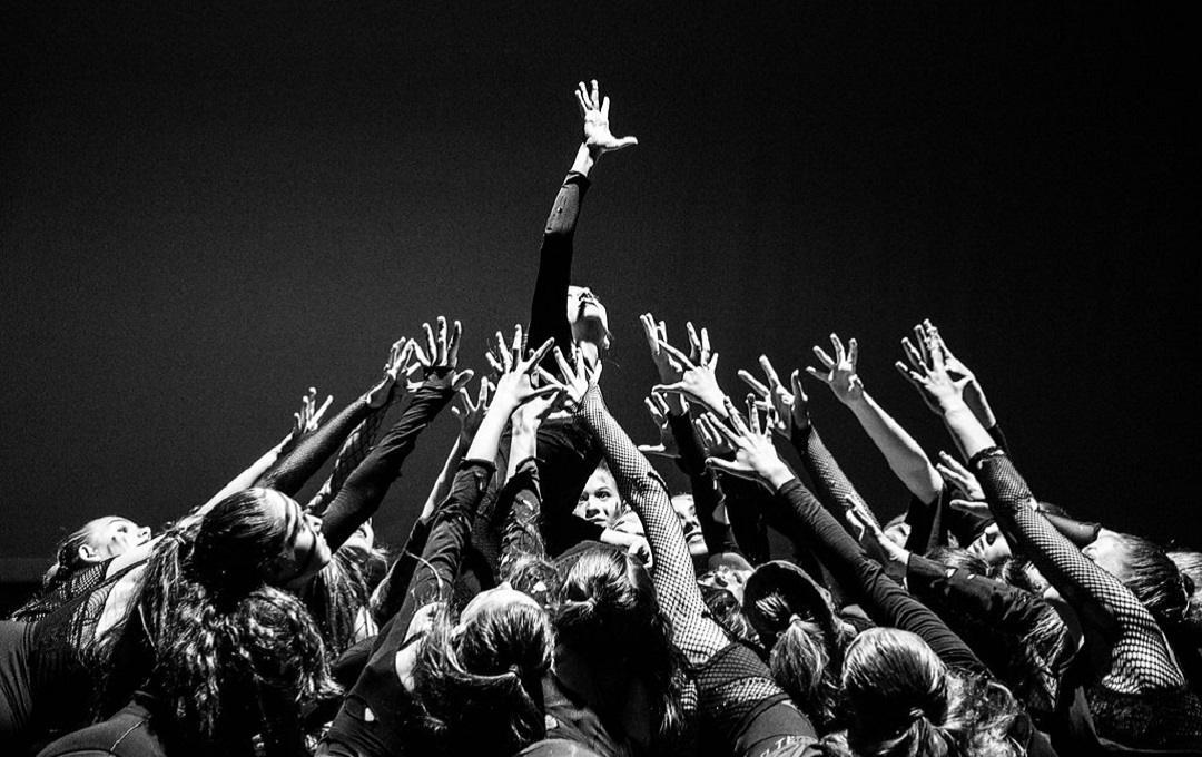 A black and white photo of dancers gathered in a group with their hands in the air.