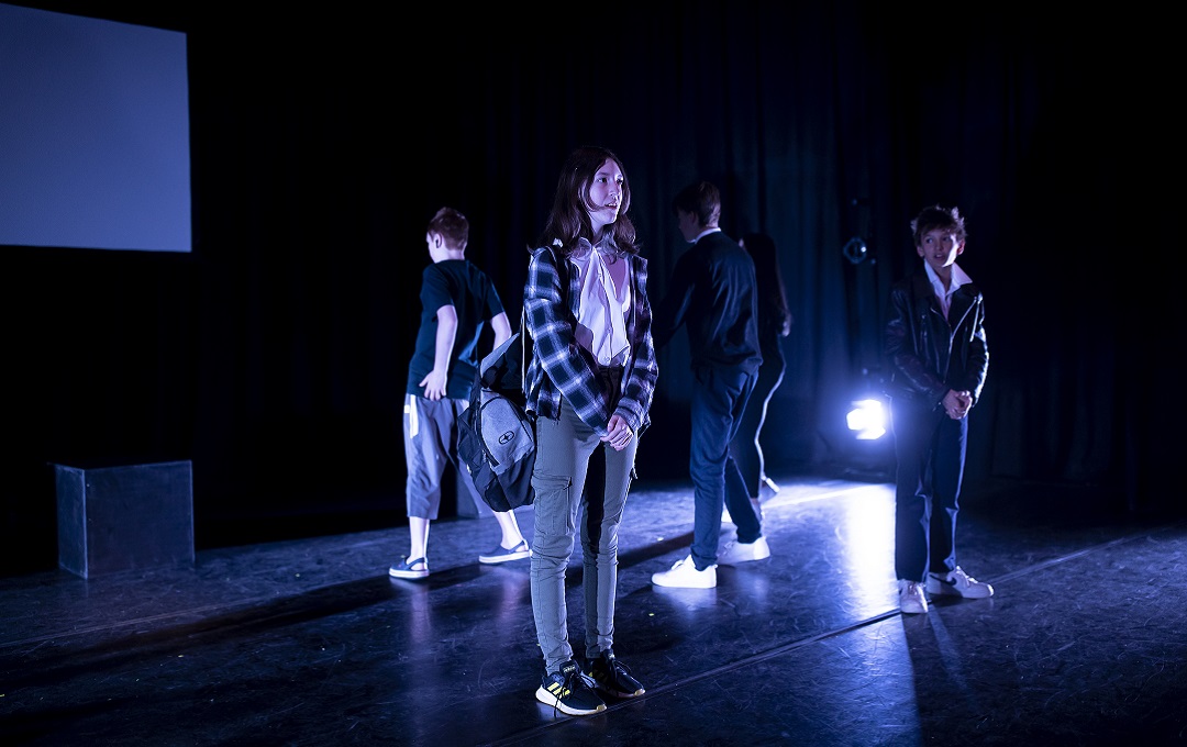 Four young people acting on stage with low lighting