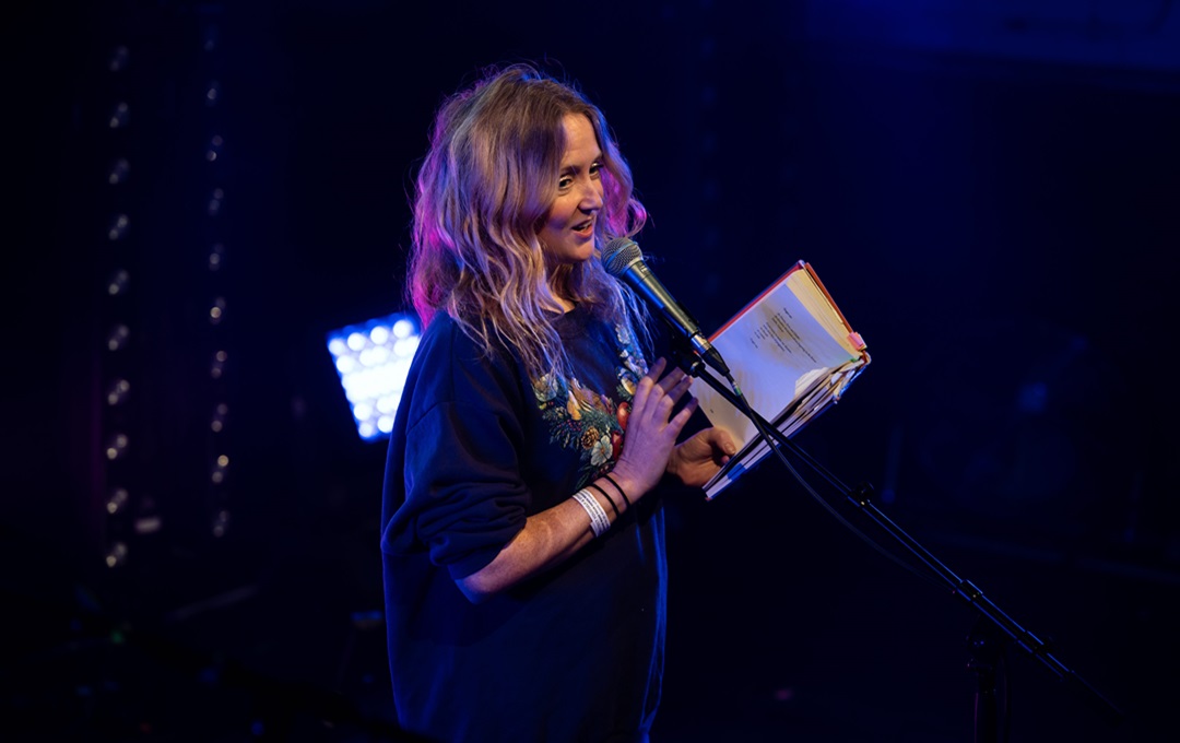 Hollie McNish reading from a book in front of a microphone