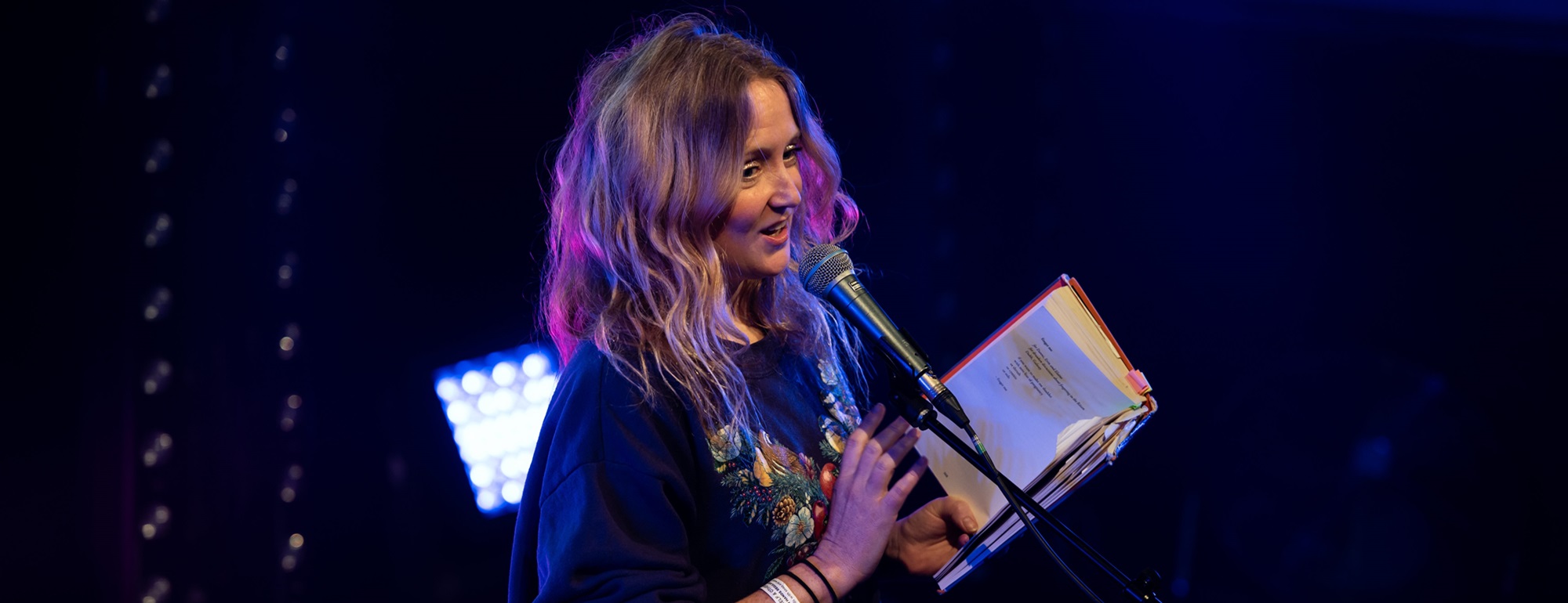 Hollie McNish reading from a book in front of a microphone