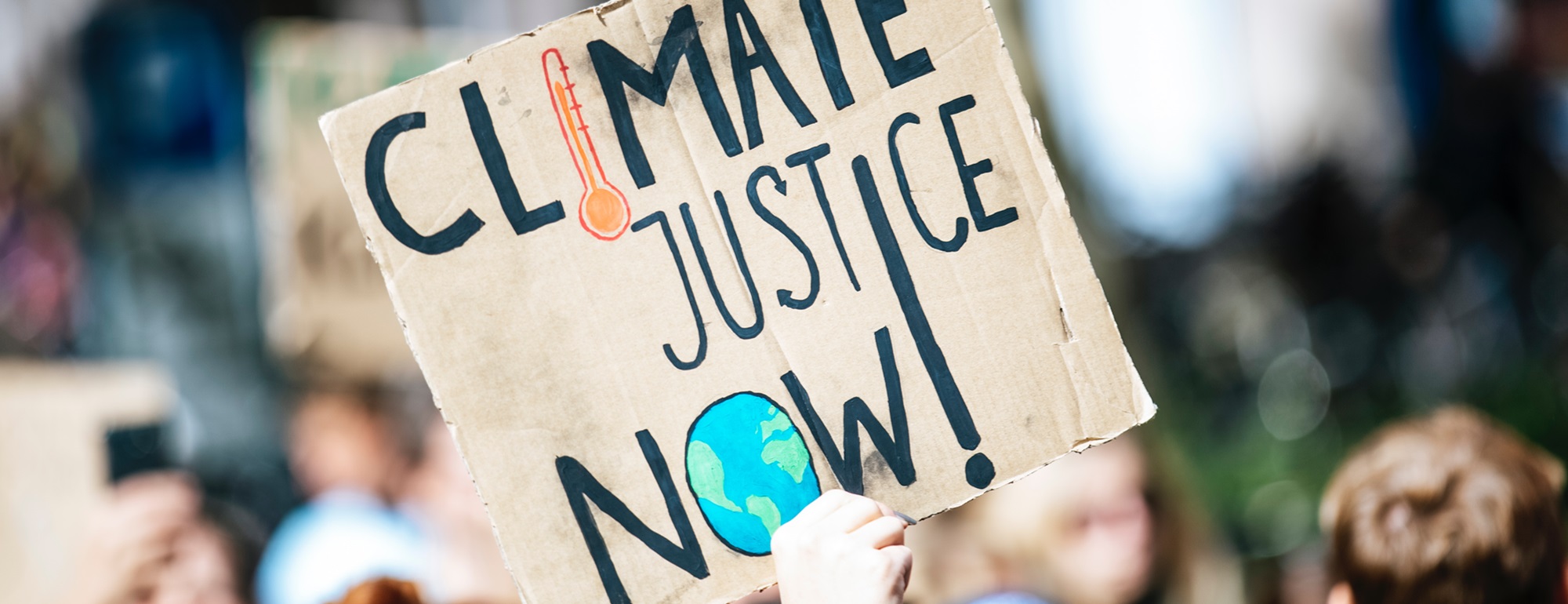 A cardboard sign with Climate Justice Now at a protest