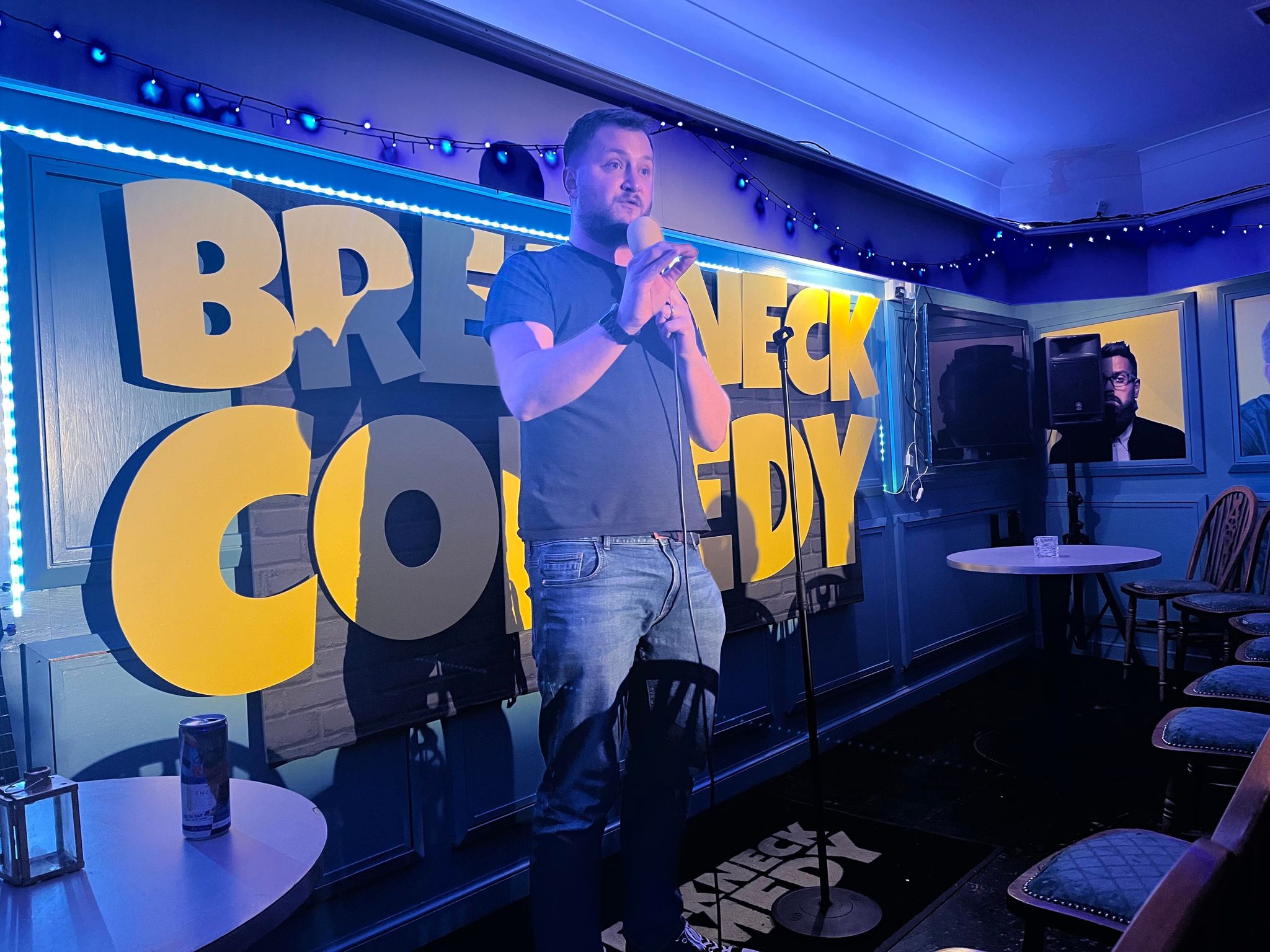 Dave Wandless performing in front of a large, yellow Breakneck Comedy sign