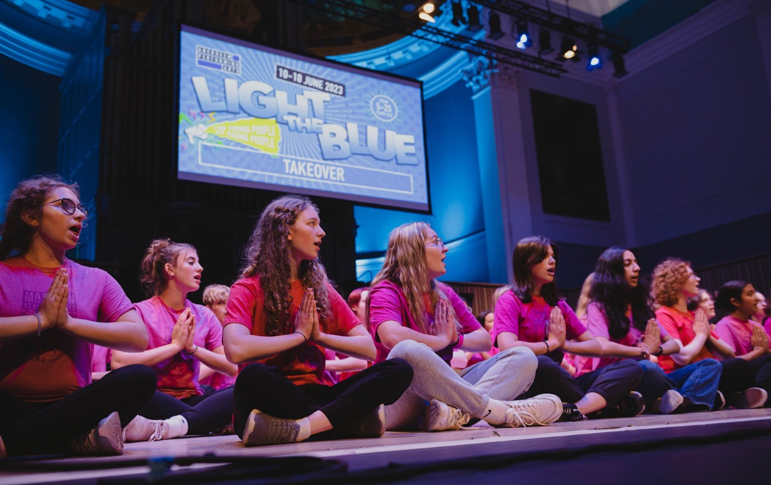 Young performers sitting on a stage underneath a Light the Blue sign